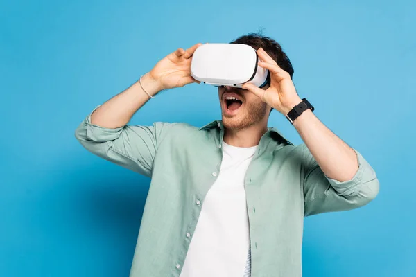 Eccitato giovane uomo utilizzando auricolare vr su blu — Foto stock