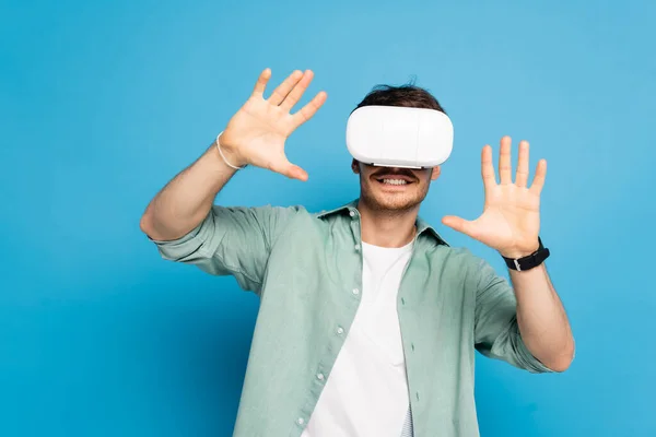 Uomo sorridente gesticolando durante l'utilizzo di auricolare vr su blu — Foto stock