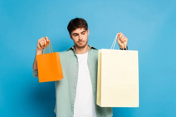 Thoughtful young man holding shopping bags on blue — Stock Photo