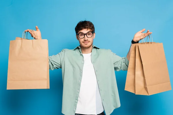 Joven guapo sosteniendo bolsas de compras en azul - foto de stock