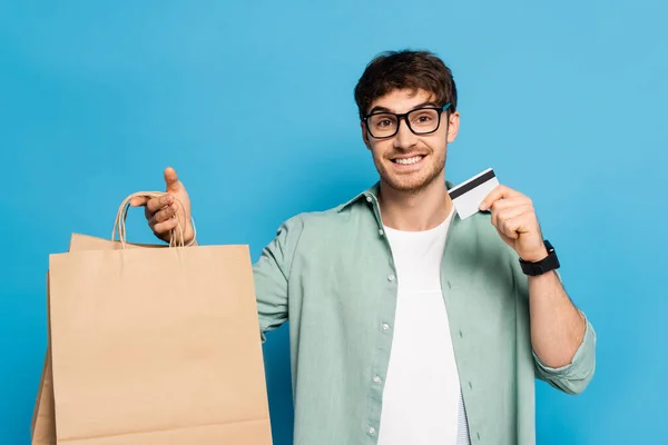 Jovem feliz mostrando saco de compras e cartão de crédito no azul — Fotografia de Stock