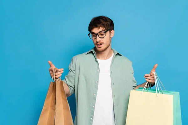 Entmutigter junger Mann mit Einkaufstüten auf blauem Grund — Stockfoto