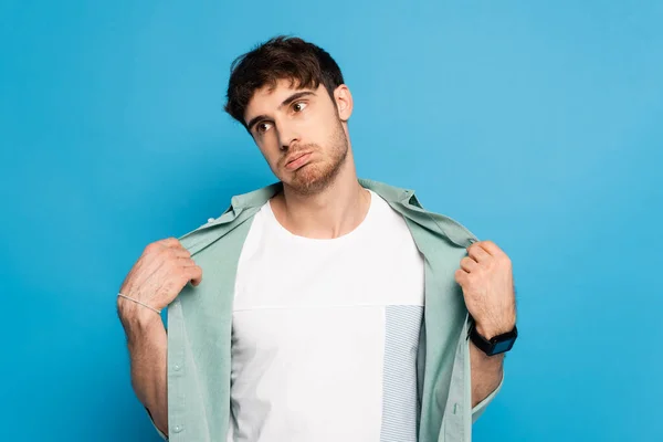 Exhausted young man touching shirt while suffering from summer heat on blue — Stock Photo