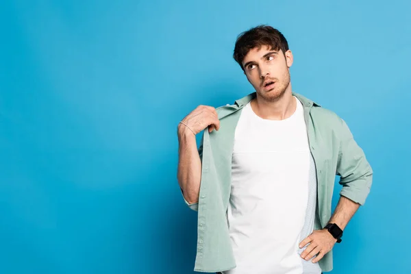 Exhausted young man touching shirt while suffering from summer heat on blue — Stock Photo