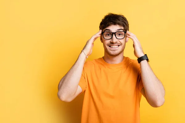 Jovem feliz tocando cabeça enquanto olha para a câmera no amarelo — Fotografia de Stock