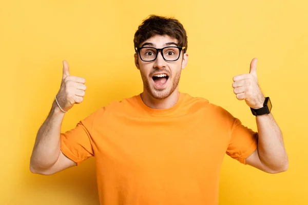 Excited young man showing thumbs up while looking at camera on yellow — Stock Photo