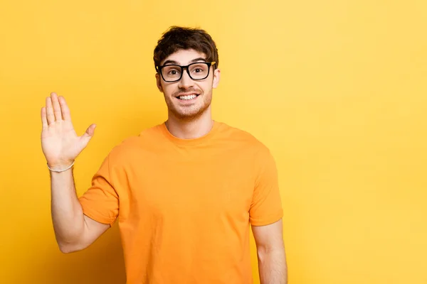 Alegre joven saludando mano mientras mira la cámara en amarillo - foto de stock