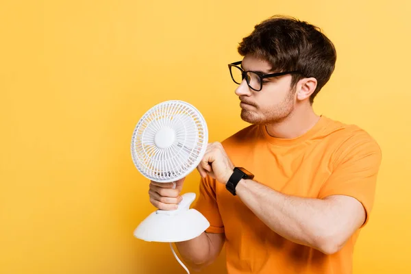 Jovem pensativo fixando ventilador elétrico no amarelo — Fotografia de Stock