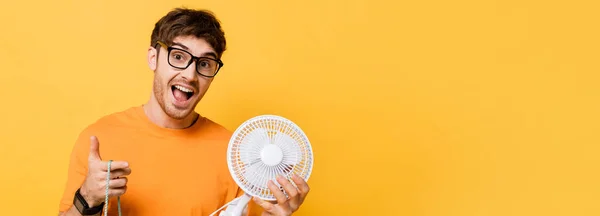 Homem animado em óculos segurando saco de compras com novo ventilador elétrico no amarelo, cabeçalho do site — Fotografia de Stock