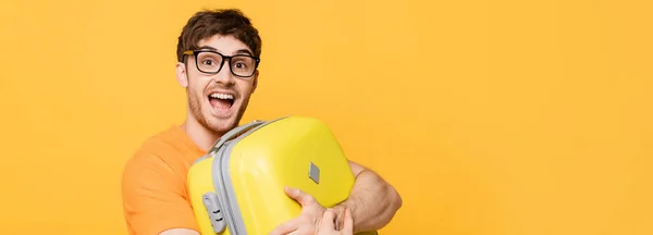 Alegre turista masculino que sostiene la maleta para las vacaciones de verano en amarillo, encabezado del sitio web - foto de stock