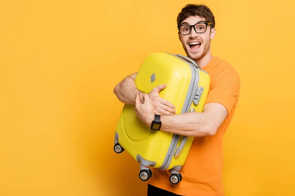 Excitado turista masculino que sostiene la maleta para las vacaciones de verano en amarillo - foto de stock