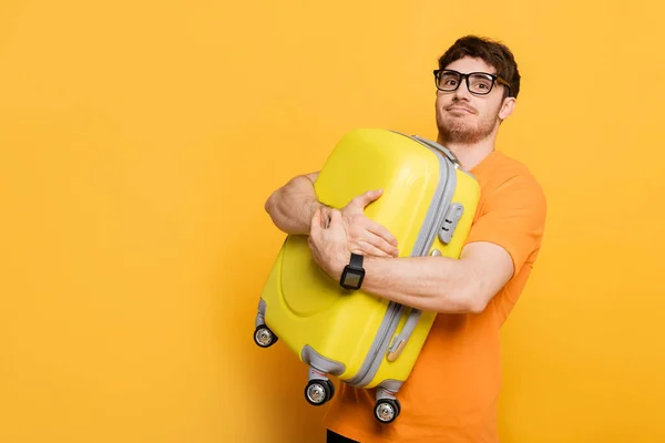 Funny male tourist holding suitcase for summer vacation on yellow — Stock Photo