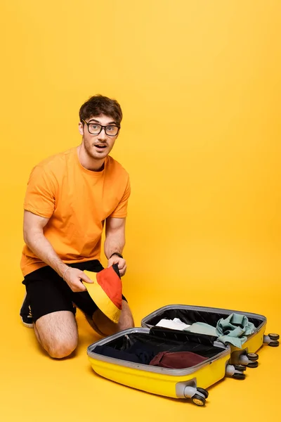 Surprised male tourist packing luggage for summer vacation on yellow — Stock Photo