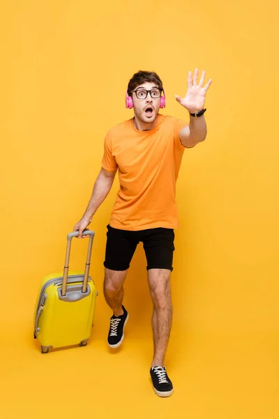 Spät schreiender Mann mit Kopfhörer läuft mit Reisetasche auf gelb — Stockfoto