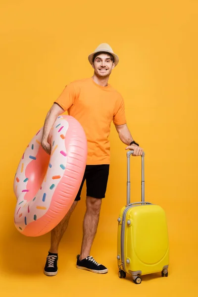 Усміхнений чоловік з валізою і надувний пончик готовий до літньої відпустки на жовтому — стокове фото