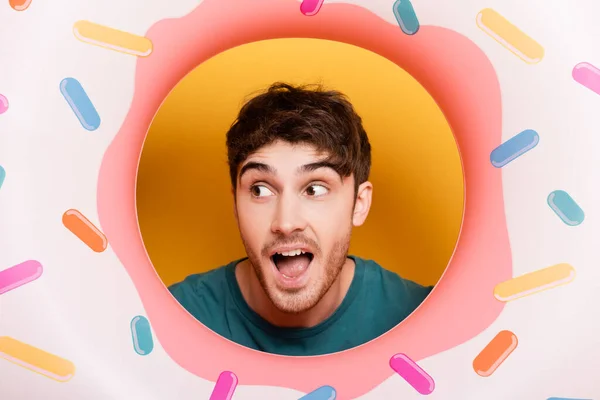 Surprised man with open mouth standing with inflatable donut on yellow — Stock Photo