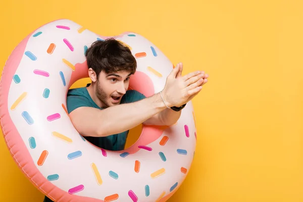 Lustiger junger Mann taucht in aufblasbaren Donut auf gelb — Stockfoto