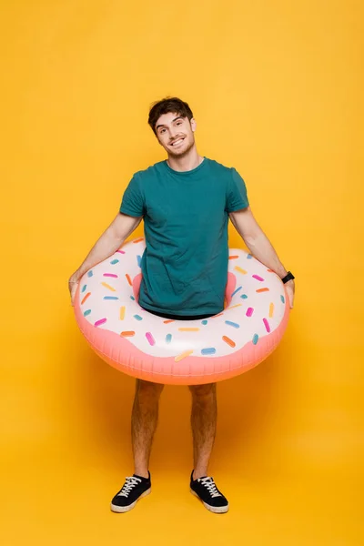 Smiling man standing with inflatable donut on yellow — Stock Photo