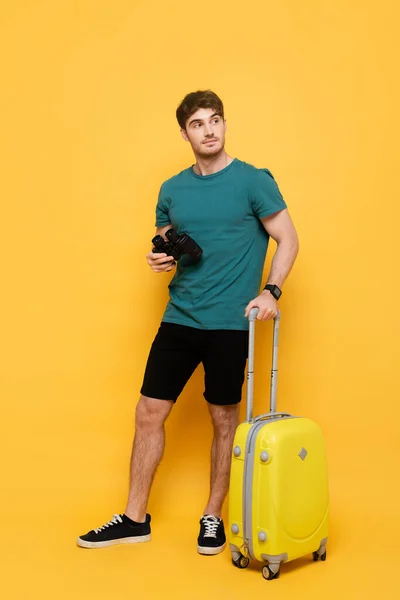 Handsome man with suitcase and binoculars ready for summer vacation on yellow — Stock Photo
