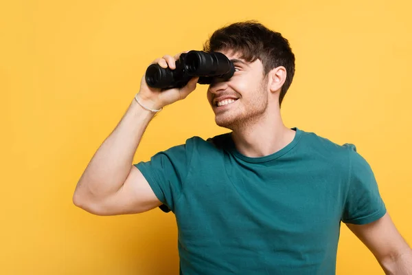 Bonito sorrindo homem olhando através binóculos no amarelo — Fotografia de Stock