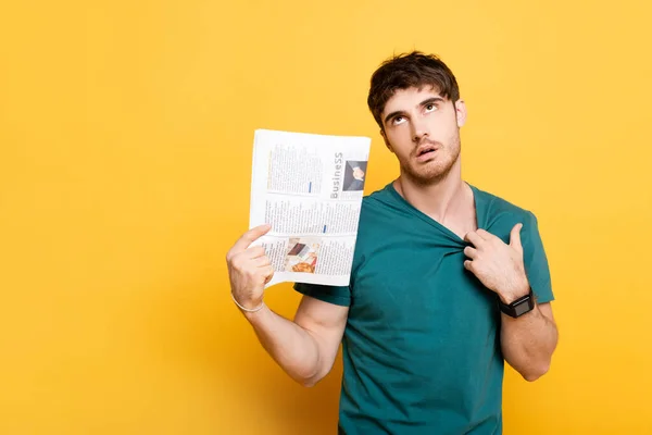 Tired man suffering from heat and using newspaper as hand fan on yellow — Stock Photo