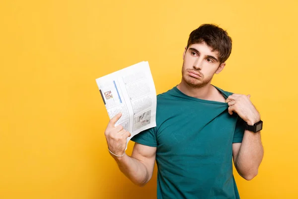 Exhausted man suffering from heat and using newspaper as hand fan on yellow — Stock Photo