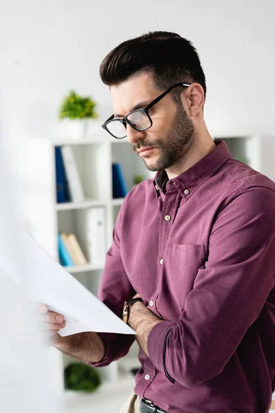Foco seletivo de homem de negócios concentrado em óculos que olha para o documento no escritório — Fotografia de Stock