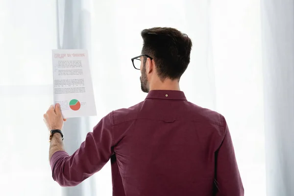 Back view of young businessman studying document with business analytics — Stock Photo