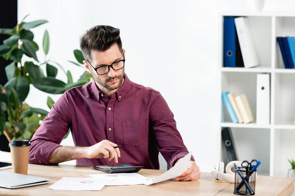 Uomo d'affari premuroso utilizzando calcolatrice mentre guardando i documenti sul posto di lavoro — Foto stock