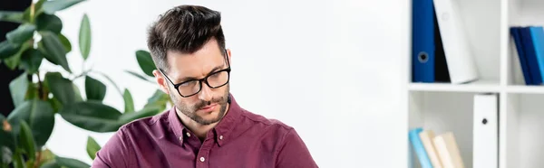 Website header of serious, thoughtful businessman working in office near potted plant — Stock Photo