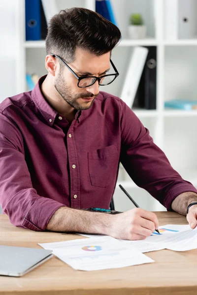 Aufmerksame Geschäftsfrau mit Brille, die am Arbeitsplatz auf Papier schreibt — Stockfoto