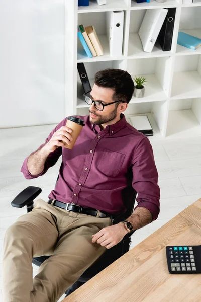 High angle view of dreamy businessman drinking coffee to go while sitting at workplace — Stock Photo