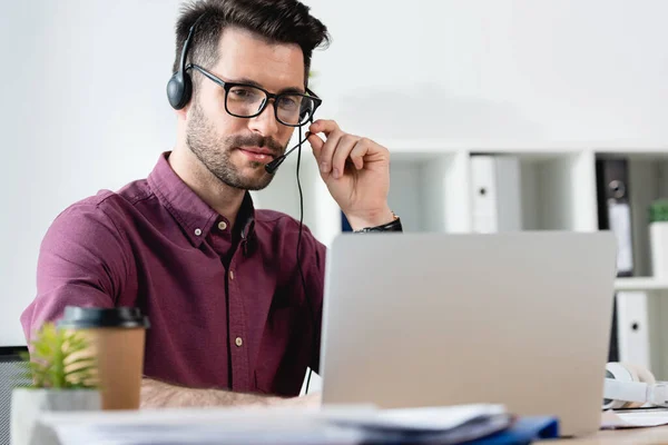 Selective focus of attentive businessman in headset looking at laptop during video call — Stock Photo