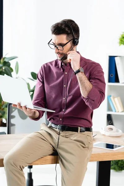 Jeune homme d'affaires dans casque tenant ordinateur portable tout en ayant appel vidéo — Photo de stock