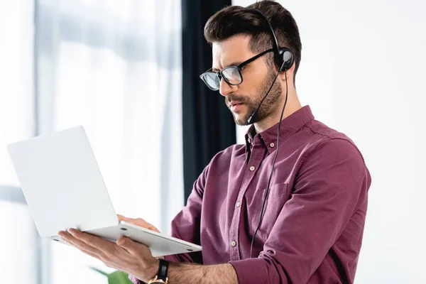 Young, serious businessman in headset holding laptop during video call on laptop — Stock Photo
