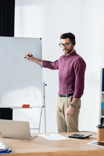 Young businessman holding felt pen near flipchart while having video conference on laptop — Stock Photo