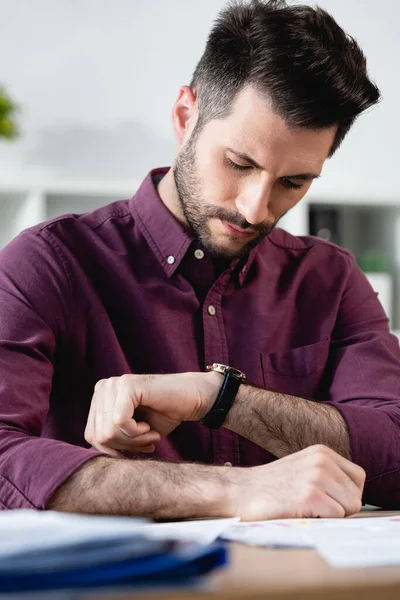 Focalizzazione selettiva di un serio uomo d'affari che controlla l'ora al polso mentre è seduto sul posto di lavoro — Foto stock