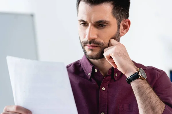 Thoughtful, serious businessman touching chin while looking at document — Stock Photo