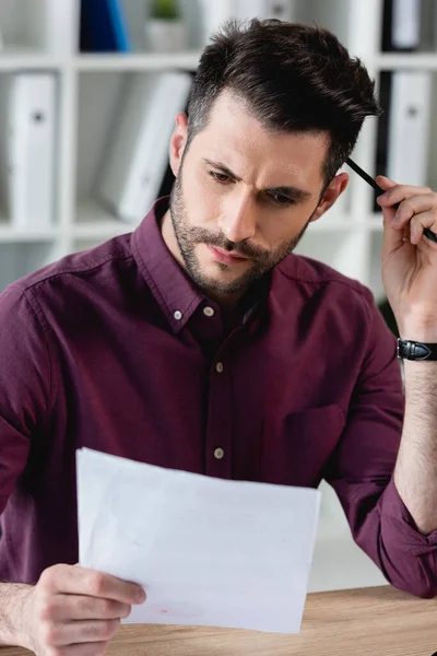 Thoughtful businessman touching head with pencil while looking at document — Stock Photo