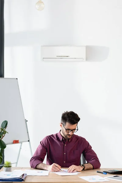 Atento hombre de negocios escribiendo en papel cerca del rotafolio mientras está sentado bajo el aire acondicionado - foto de stock