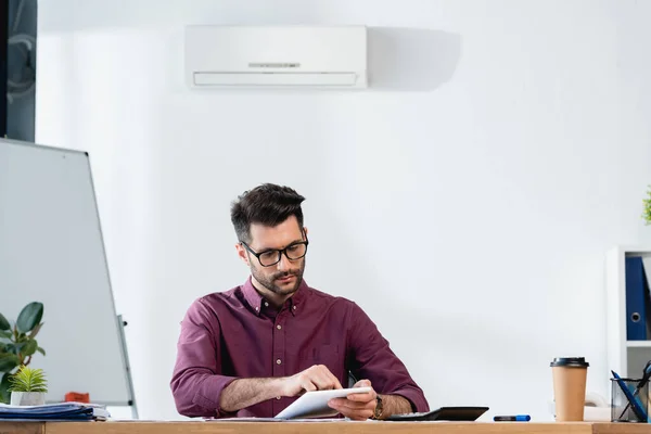Handsome businessman using digital tablet while sitting at workplace under air conditioner on wall — Stock Photo