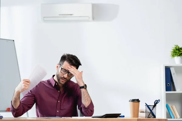 Exhausted businessman touching forehead and waving paper while suffering from heat in office — Stock Photo