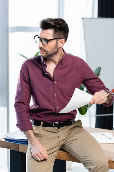 Exhausted businessman sitting on desk and waving paper while suffering from heat in office — Stock Photo
