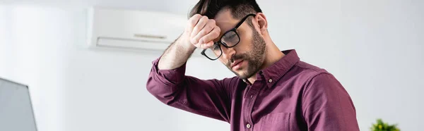 Panoramic shot of displeased businessman touching forehead while suffering from heat in office — Stock Photo