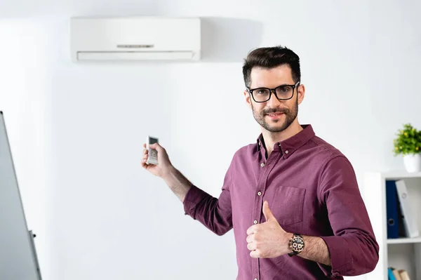 Homme d'affaires souriant montrant pouce levé tout en allumant le climatiseur avec télécommande — Photo de stock