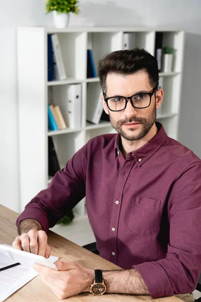 Young, confident businessman in eyeglasses looking at camera while using digital tablet — Stock Photo