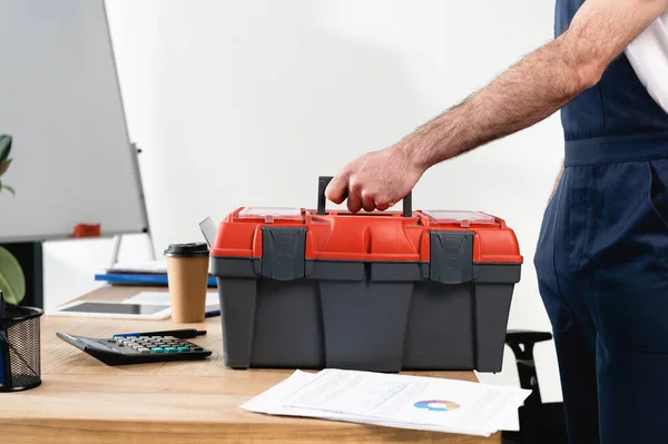 Vista cortada do reparador com caixa de ferramentas na mesa de escritório com papéis e café para ir — Fotografia de Stock