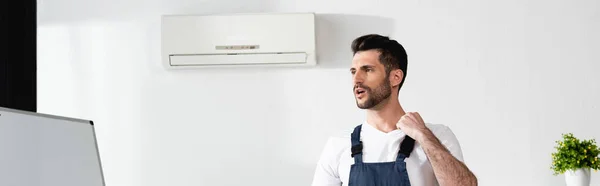 Raccolto panoramico di riparatore in piedi con cassetta degli attrezzi vicino condizionatore d'aria rotto e affetto da calore — Foto stock