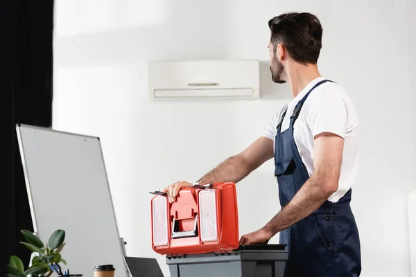 Reparador de apertura de caja de herramientas y mirando el acondicionador de aire roto en la pared - foto de stock