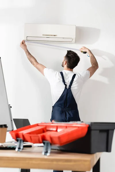 Selectiive focus of repairman measuring air conditioner near office desk with toolbox — Stock Photo